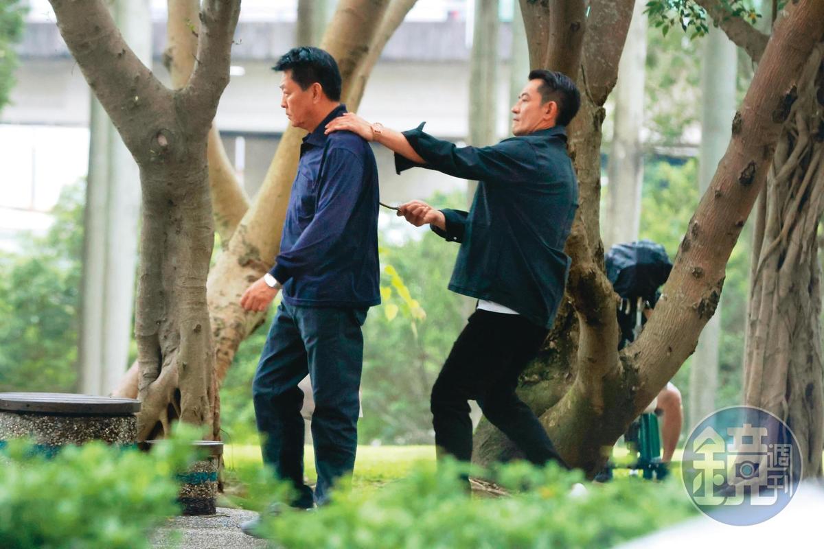 15：58，柯叔元（右）拿了樹枝從背後頂著庹宗華（左），像是在威脅他，兩人正拍攝衛視新戲。（圖／鏡週刊提供）